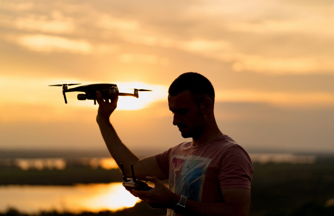 Silhouette of man piloting a drone at sunset with sunny sky in background